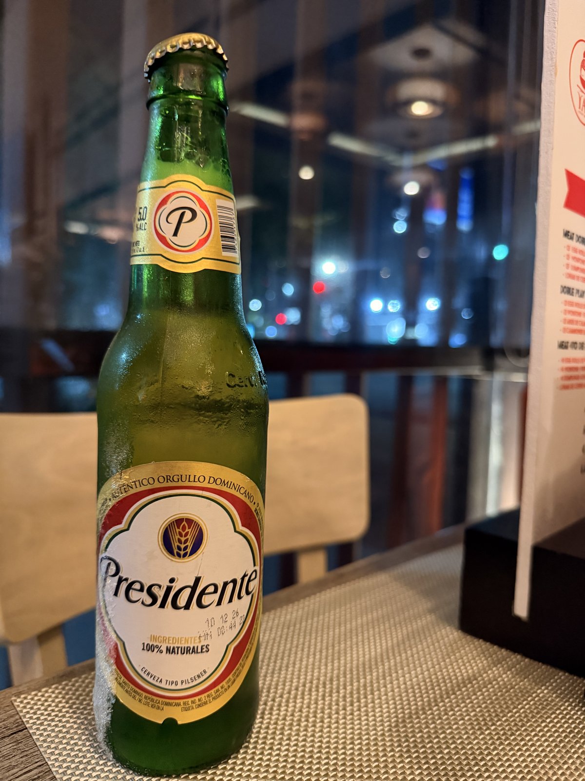 A well-chilled green bottle of Presidente on a restaurant table at night